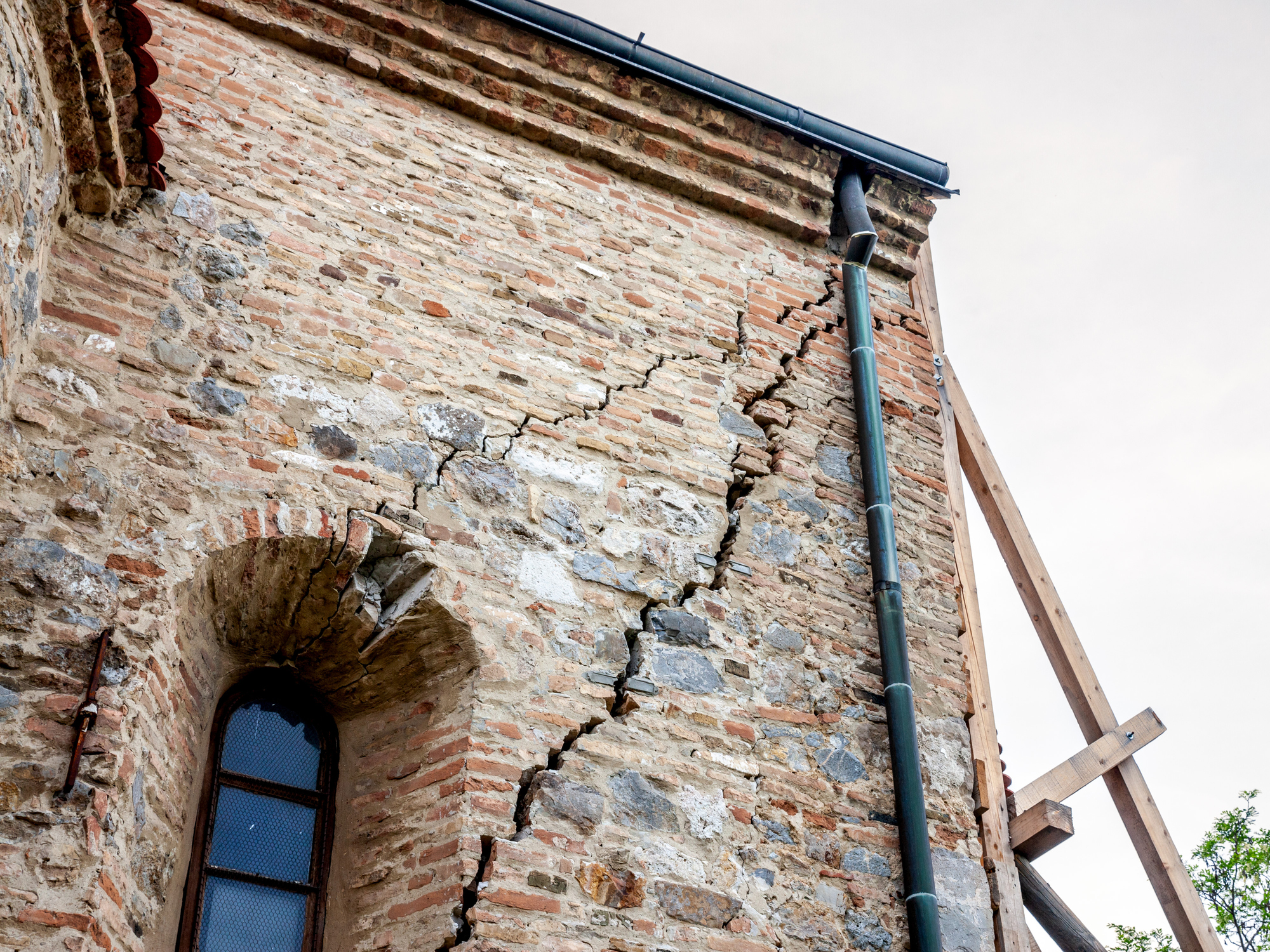 Cracked facadeof a stone wall of an old and decaying building, heavily needing renovation to avoid complete collapse and destruction.